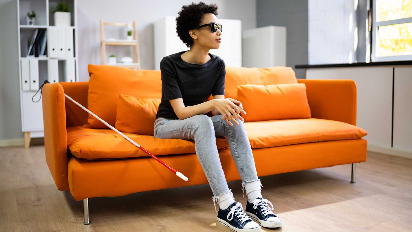 Visual Disabilities - Person with visual impairment sitting on orange sofa in office setting with white cane